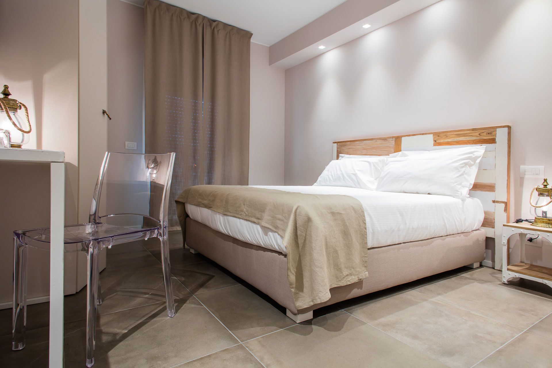 A modern hotel room with a bed, a nightstand, a clear chair, and a curtain.