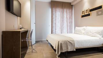 A bedroom with a bed, a desk, a chair, a TV, and a window with curtains.