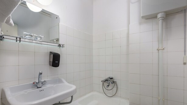 A bathroom with a white sink, a mirror, a soap dispenser, a bathtub, and a toilet. - Boarding House Lucija (Kostrena)