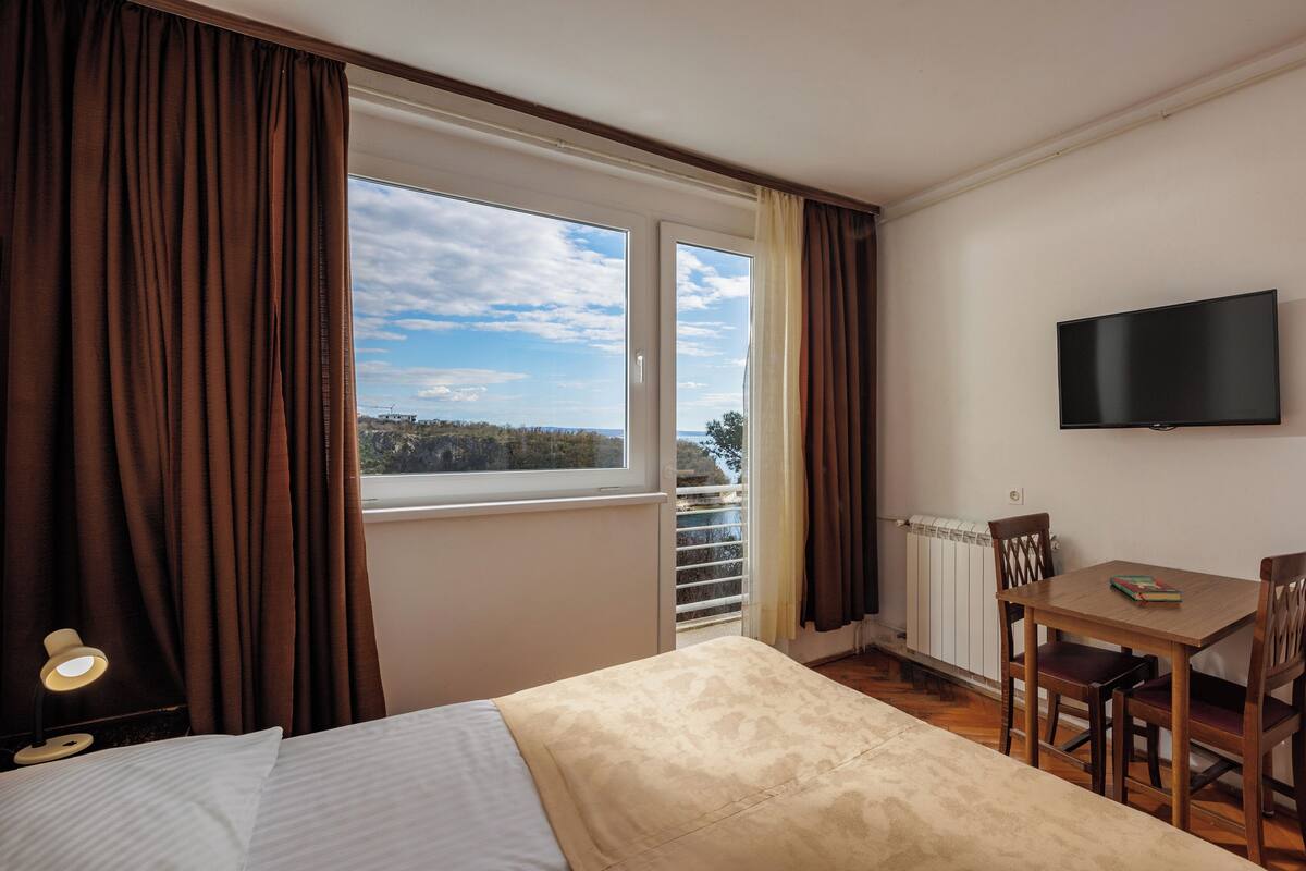 A hotel room with a bed, a table with chairs, a TV, and a view of the outdoors.