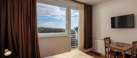 Una habitación de hotel con cama, una mesa con sillas, televisión y vistas al exterior.