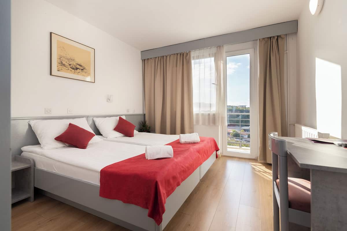 A hotel room with a bed, a desk, and a view of the city.