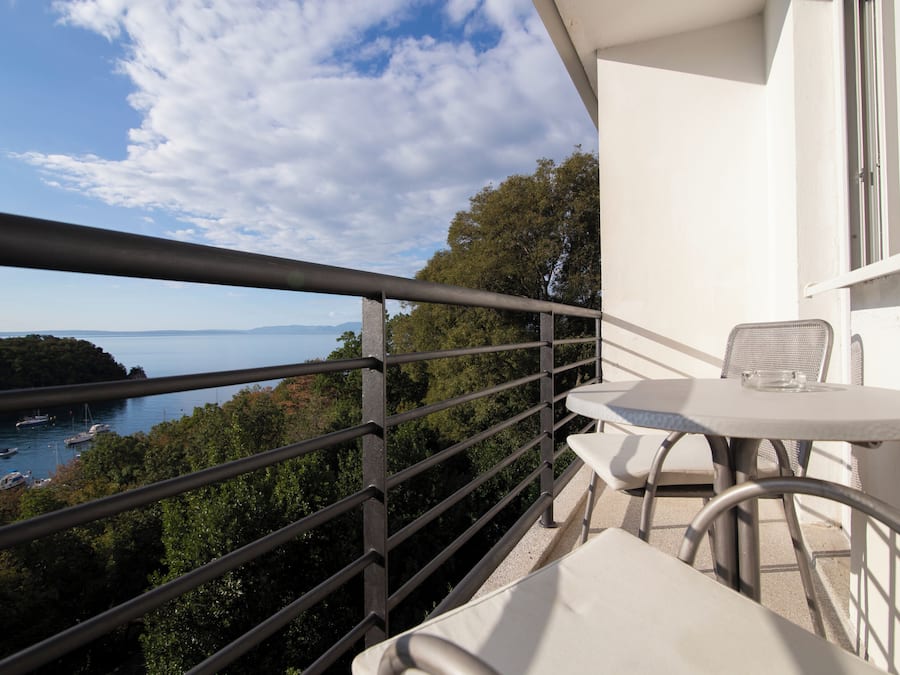 Een balkon met een tafel en stoelen, met uitzicht op een baai vol boten en begroeiing.