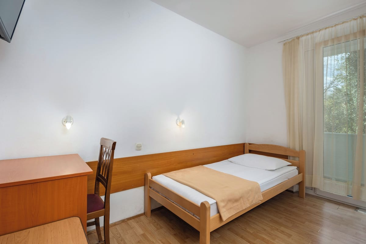 A room with a wooden bed, a wooden desk, a chair, and two wall-mounted lights.