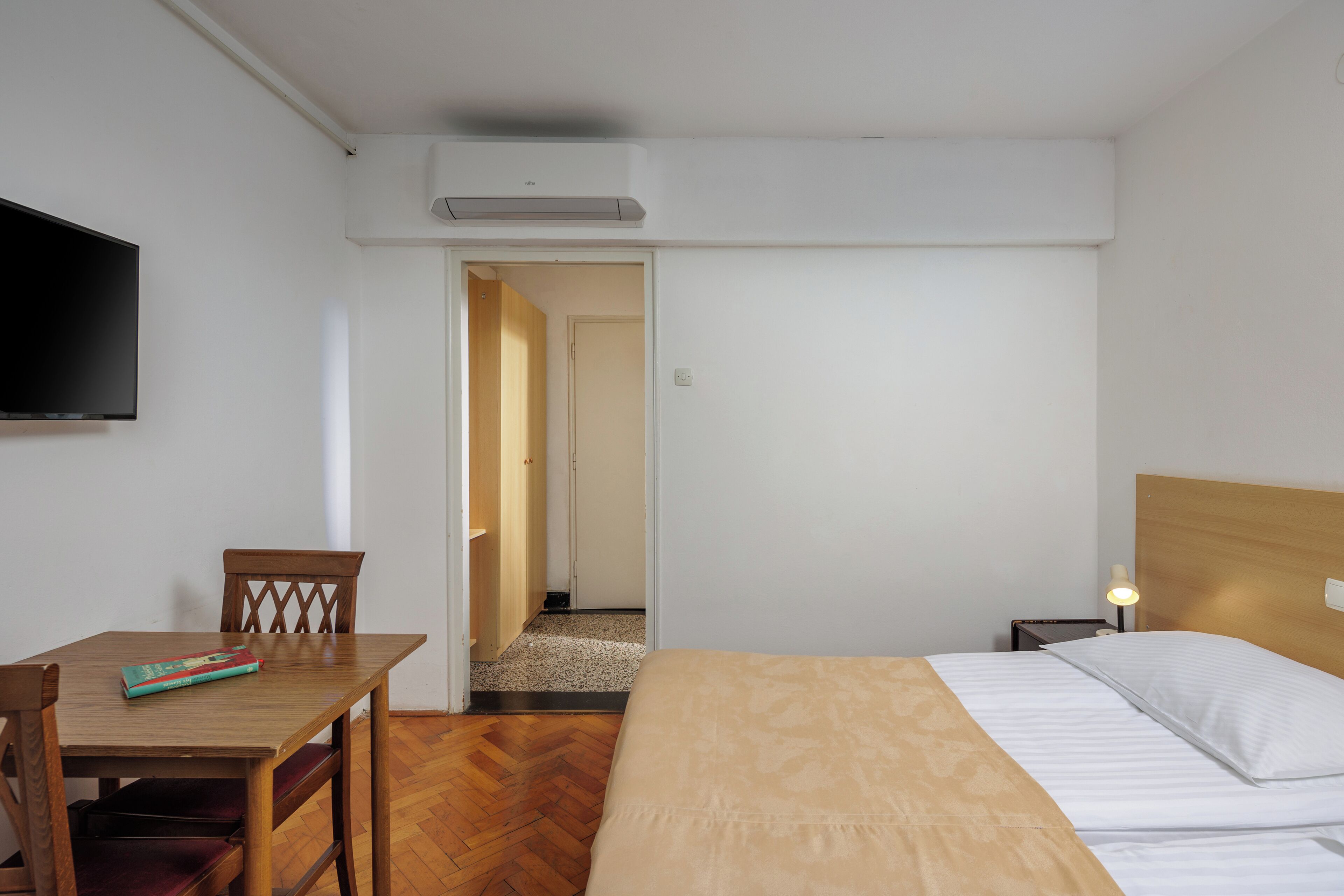 Een hotelkamer met een bed, een bureau met stoel, een aan de muur bevestigde televisie en een airconditioning.