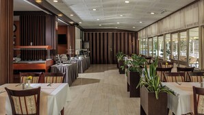 A restaurant with a long counter, multiple tables, and chairs. There are potted plants and a large window with a view. - Boarding House Lucija (Kostrena)