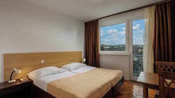 A hotel room with a bed, bedside table, lamp, and a view of the city through a window.