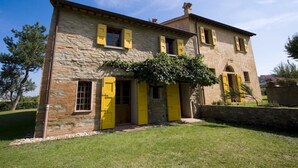Un edificio de piedra con contraventanas amarillas, una entrada central y un pequeño jardín.