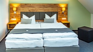 Ein Hotelzimmer mit einem hölzernen Kopfteil, zwei Nachttischen mit Lampen, einem Bett mit weißer Bettwäsche und einer grauen Bank.
