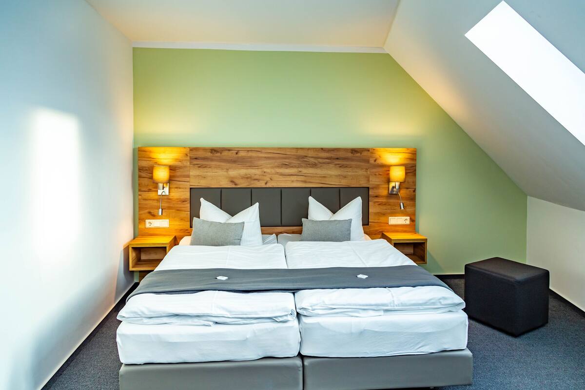 Een moderne hotelkamer met een groot bed, een houten hoofdbord en twee bedlampjes.