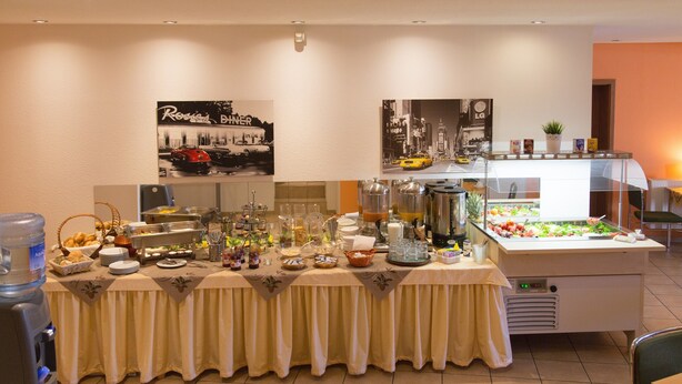 Ein reichhaltiges Buffet mit verschiedenen Speisen und Getränken, einem Wasserspender und einem Kühlschrank.