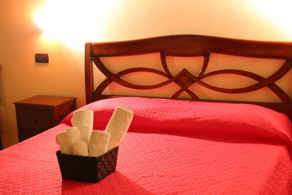 Un letto con una coperta rossa e un cesto di asciugamani bianchi.