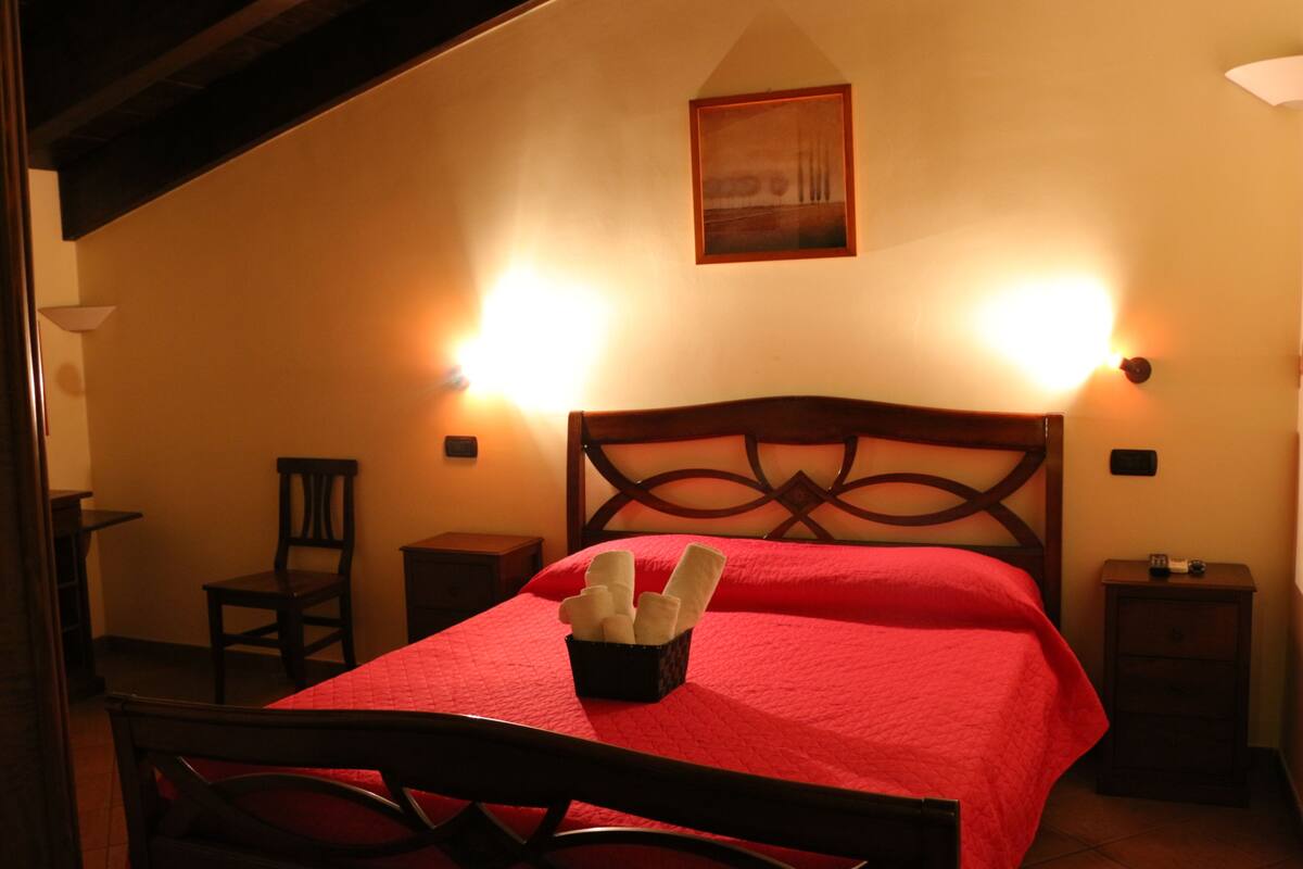 Ein Schlafzimmer mit einem hölzernen Bett, roter Bettwäsche, einem Nachttisch, einem Stuhl und zwei Wandleuchten.