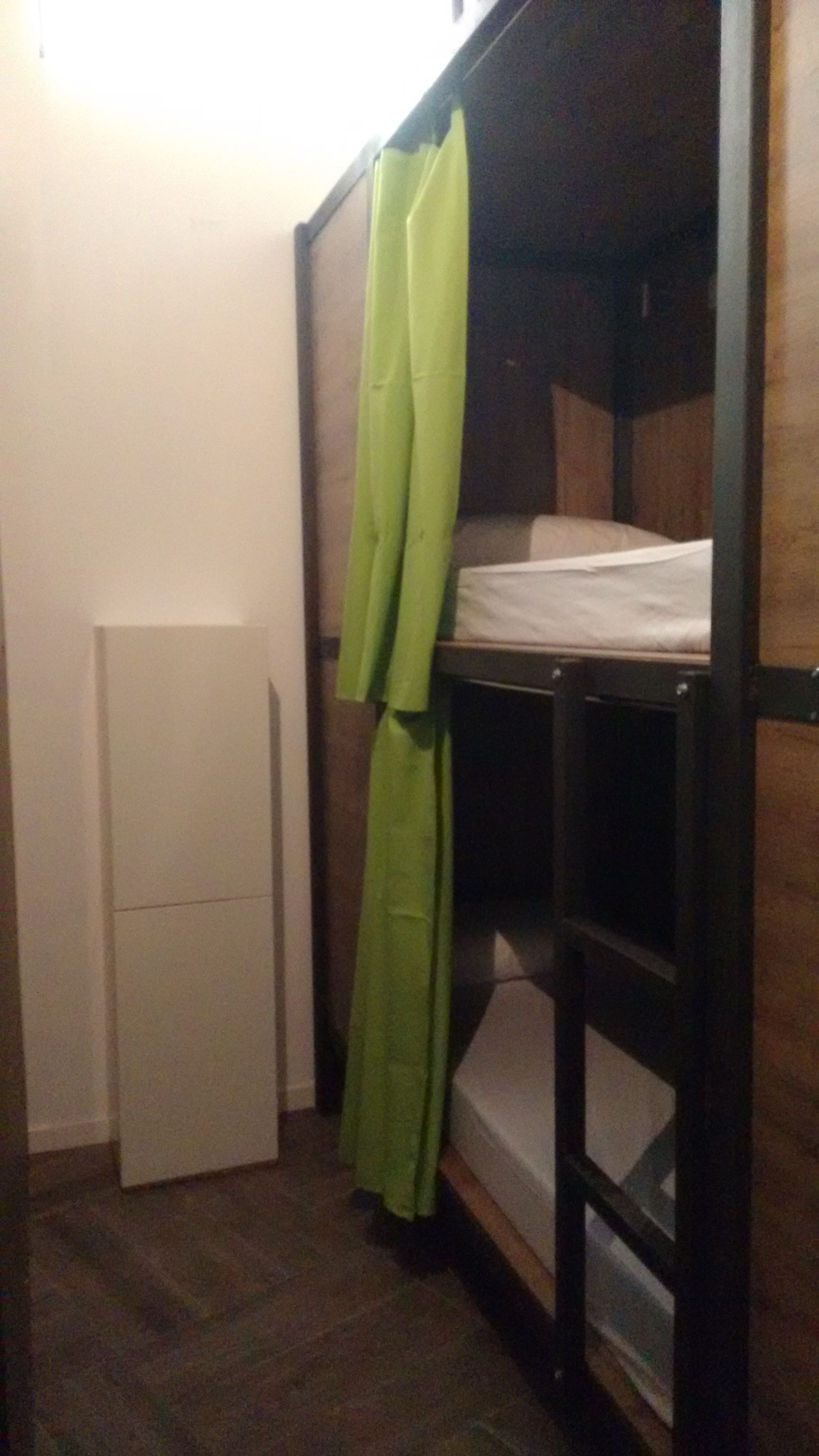 Ein kleiner, kompakter Raum mit einem Etagenbett, einem weißen Kühlschrank und einem grünen Vorhang.