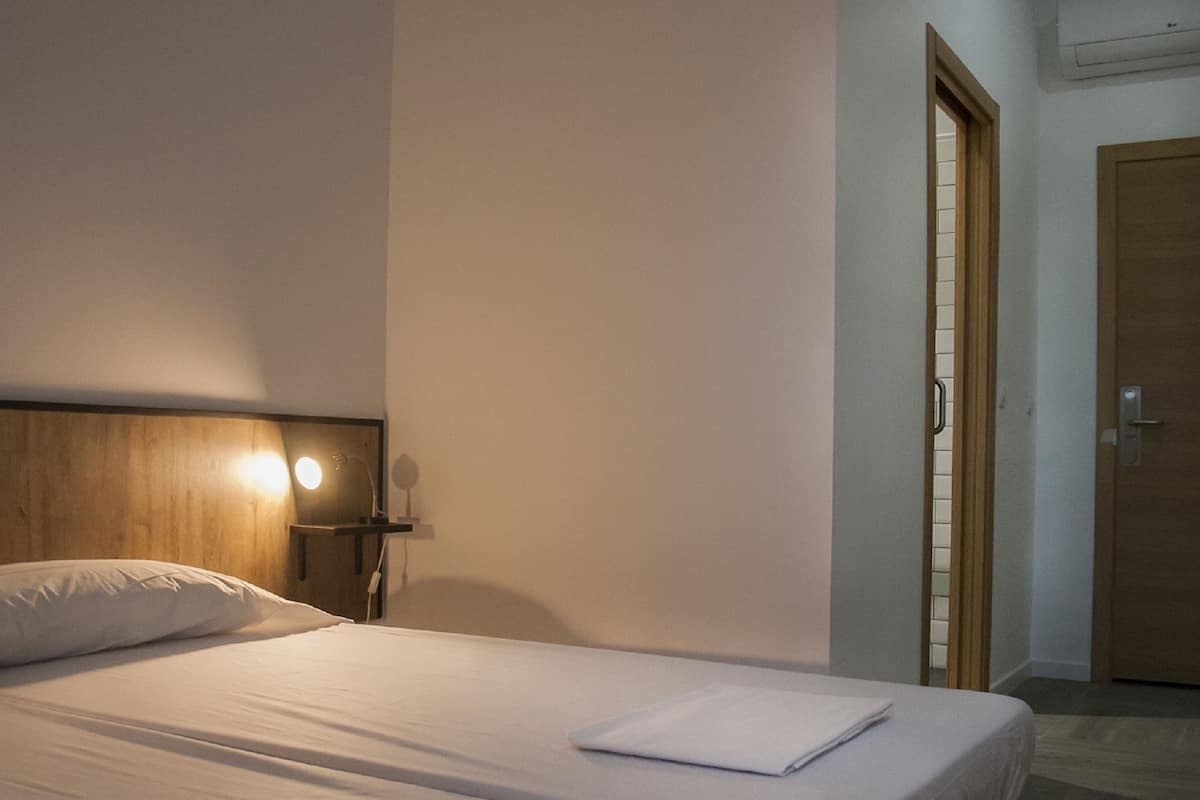 Ein Hotelzimmer mit zwei Betten, einem Holzkopfteil, einem Nachttisch mit Lampe und einer Tür mit Griff.