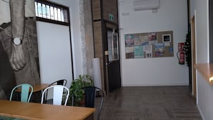 Une salle de conférence avec une table en bois, des chaises, une plante en pot, un tableau d’affichage où sont accrochées diverses annonces, et une porte avec une pancarte indiquant « SORTIE ».