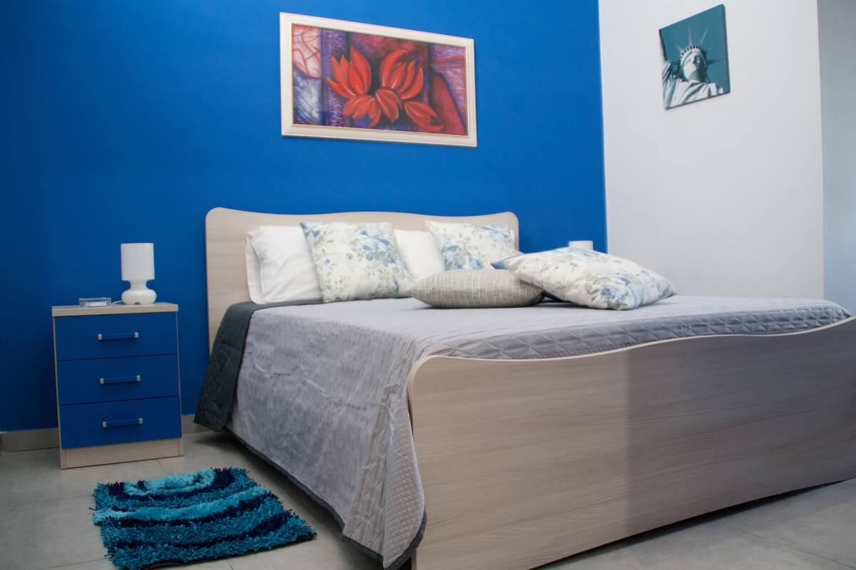 Une chambre à coucher avec un lit, une table de chevet, une lampe et un tapis bleu.
