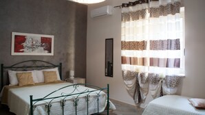 A bedroom with a bed, bedside table, and a window with patterned curtains. - The Liberty Palace b&b (Campobello di Licata)