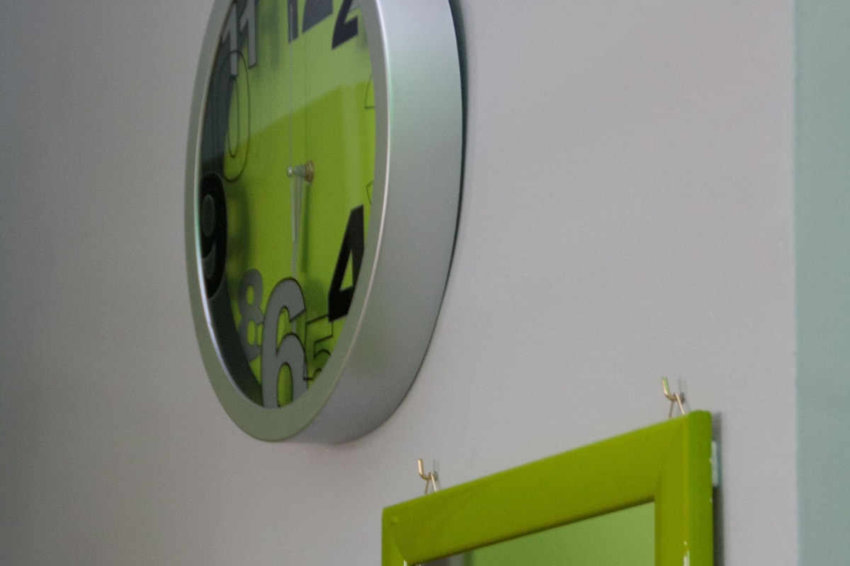 Une horloge murale avec un cadre vert et un miroir placé en dessous.