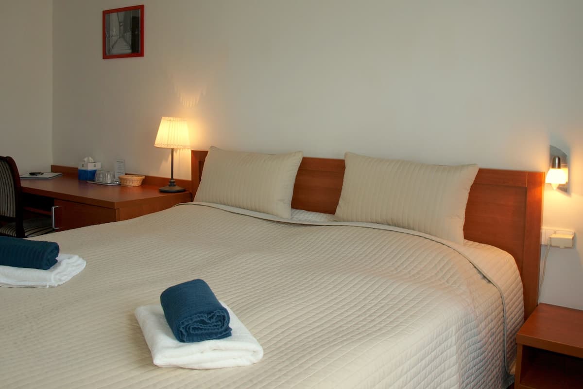 Ett hotellrum med en säng, ett skrivbord, en stol, en lampa och ett nattduksbord.