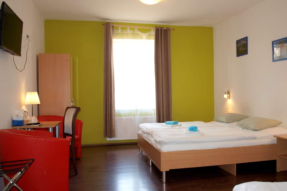 Ett hotellrum med en säng, ett skrivbord, en stol, ett fönster med gardiner och en tv som är monterad på väggen.
