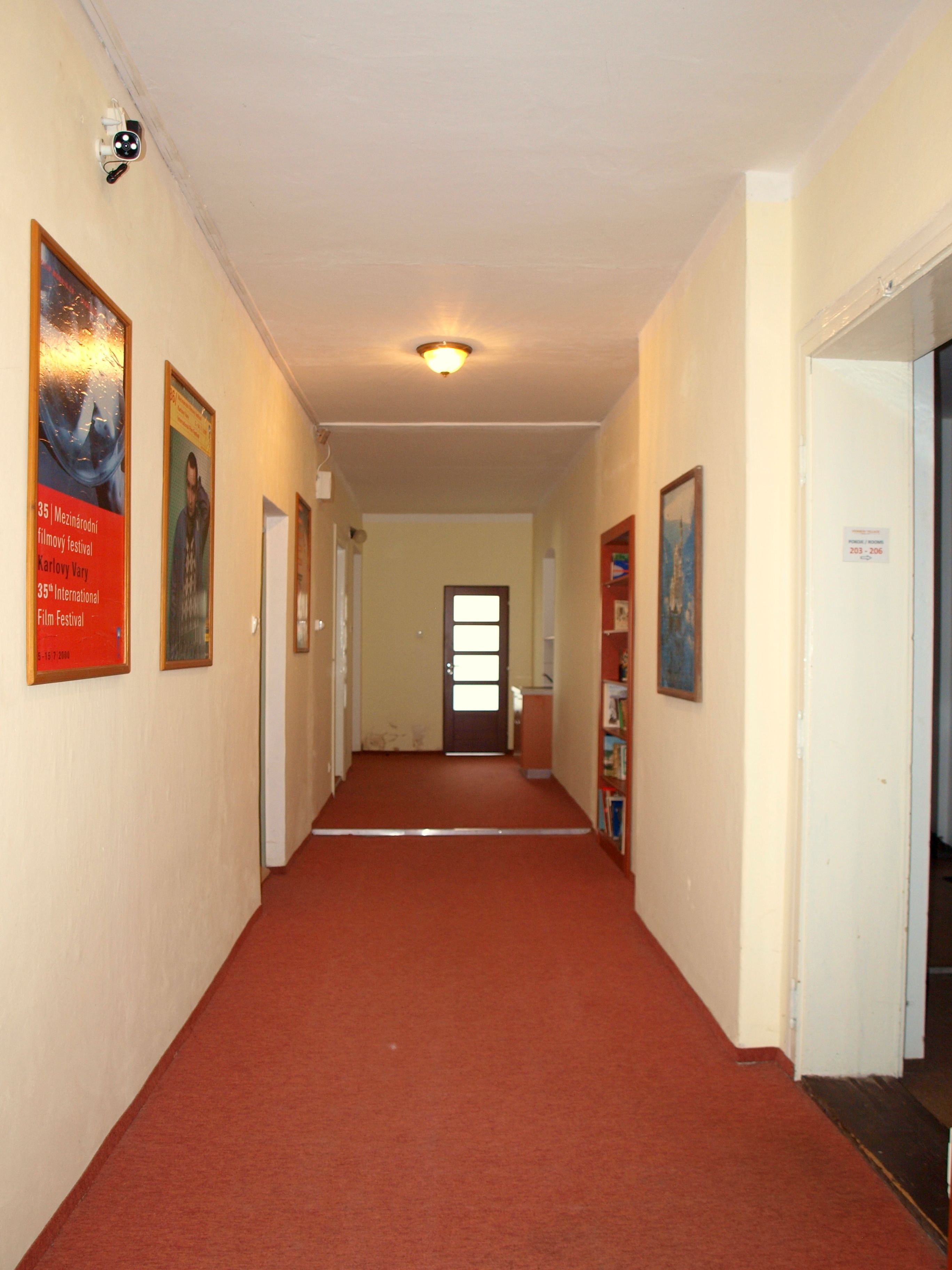 Een gang met een rode tapijten, witte muren en inlijste foto's aan de wand.
