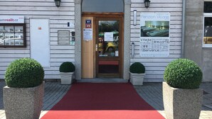 A building entrance with a red carpet, two potted plants, and signs in multiple languages. - Penzion Village (Karlovy Vary)