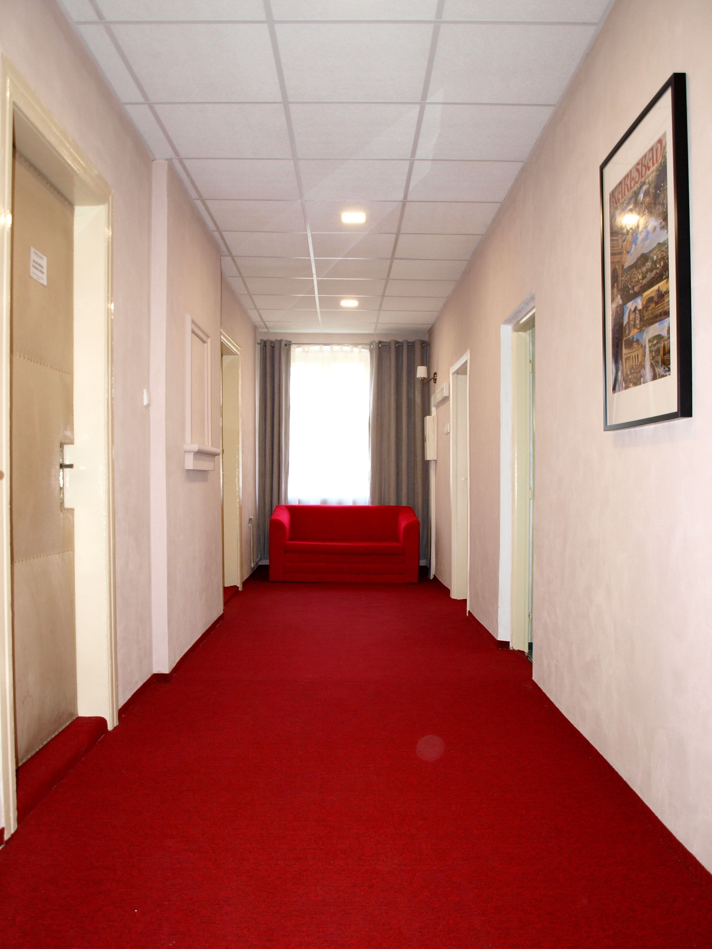 Un pasillo con alfombra roja, un sofá rojo y un cuadro enmarcado en la pared.