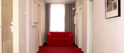 Un pasillo con alfombra roja, un sofá rojo y un cuadro enmarcado en la pared.