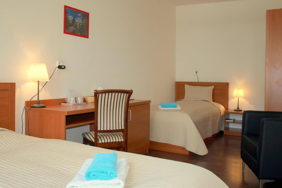 Ett hotellrum med två sängar, ett skrivbord, en stol och ett litet bord med en lampa.