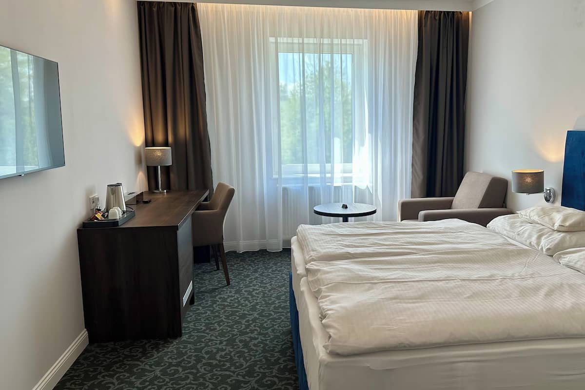 Ett hotellrum med en säng, ett skrivbord, en stol, ett litet bord och en tv.