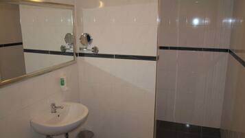 A bathroom with a sink, mirror, and shower area.