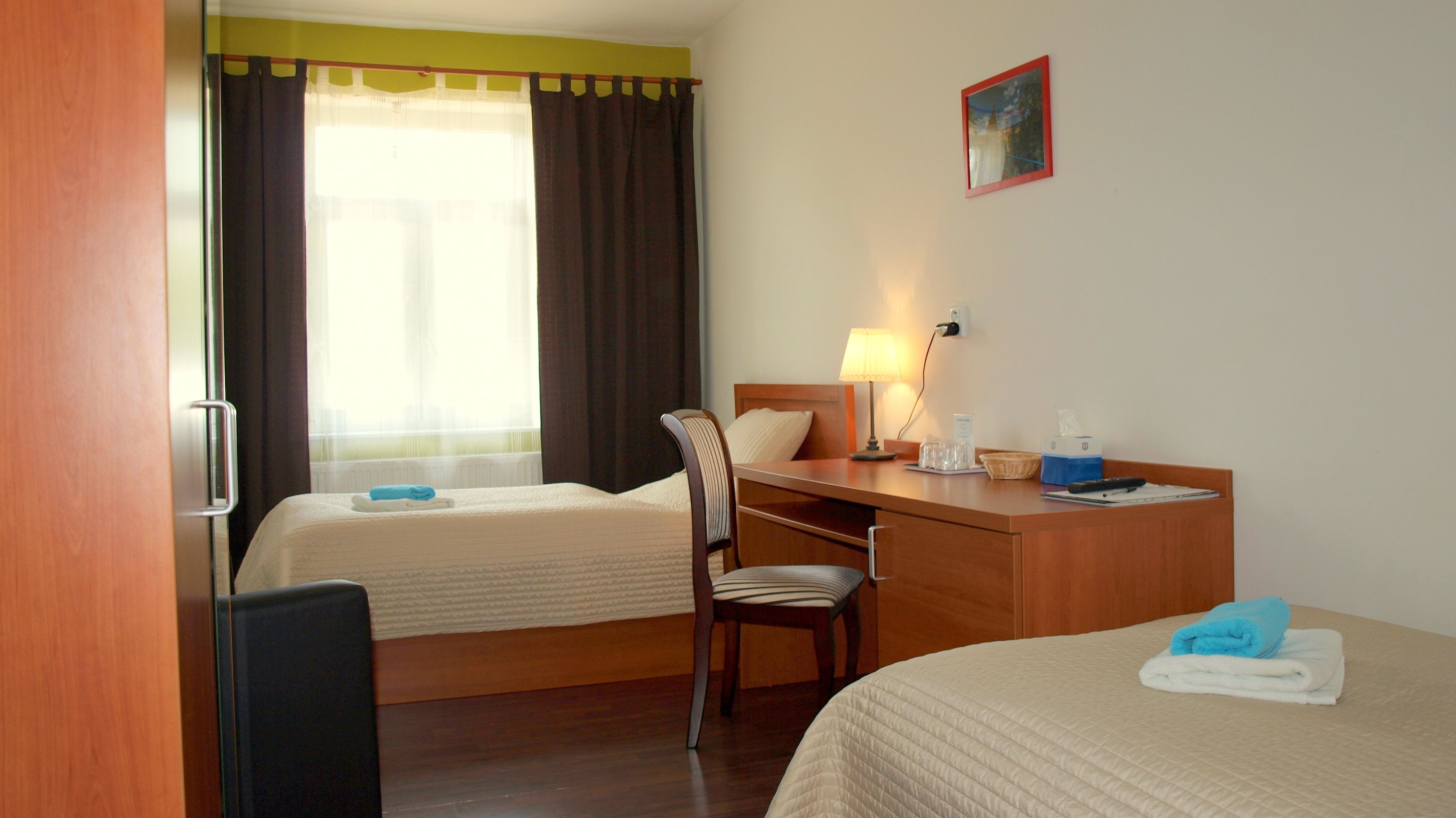 Une chambre d’hôtel avec deux lits, un bureau, une chaise, une lampe et une fenêtre avec des rideaux.