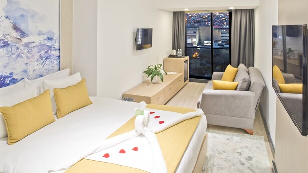 Une chambre d’hôtel avec un lit, un canapé, une télévision et une fenêtre donnant sur la ville.