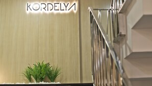 Une enseigne portant le nom « KORDELYA » est fixée à un mur et illuminée, à côté d’un escalier doté de rampes en métal.