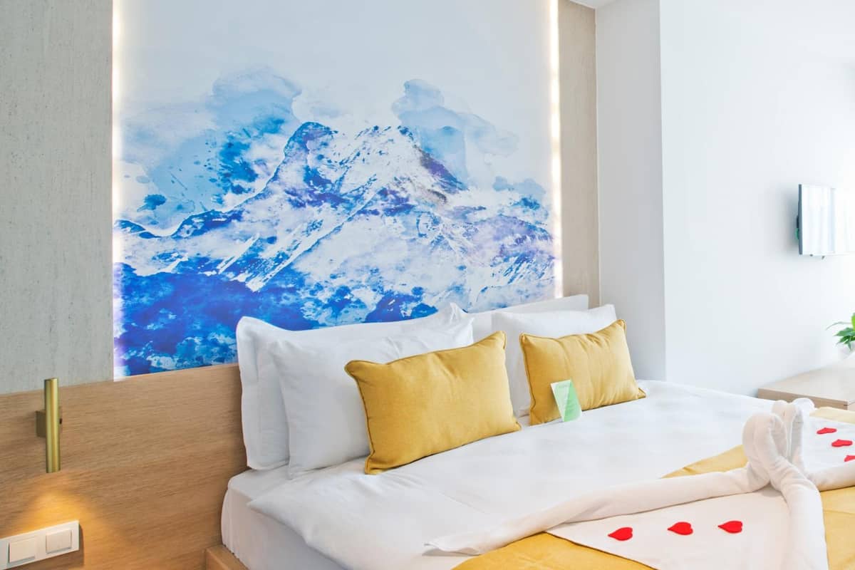 A hotel room with a bed, white bedding, a wooden headboard, and a large abstract painting on the wall.