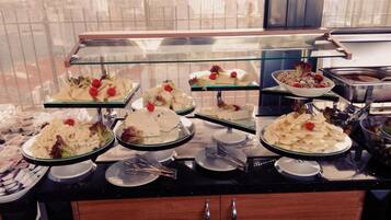 A buffet with various dishes, including salads, fruits, and desserts, displayed on glass shelves.