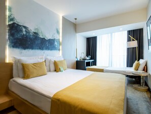 Ein Hotelzimmer mit einem großen Bett, einem Schreibtisch und Blick auf die Stadt.