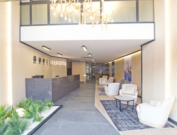 A hotel reception area with a marble counter, seating area with white chairs, a reception desk, and a modern chandelier.