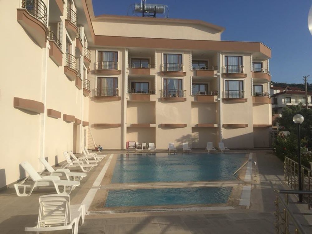 A hotel with a swimming pool, multiple balconies, and lounge chairs.