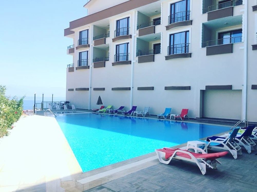 A poolside area with lounge chairs, a pool, and a building with balconies.