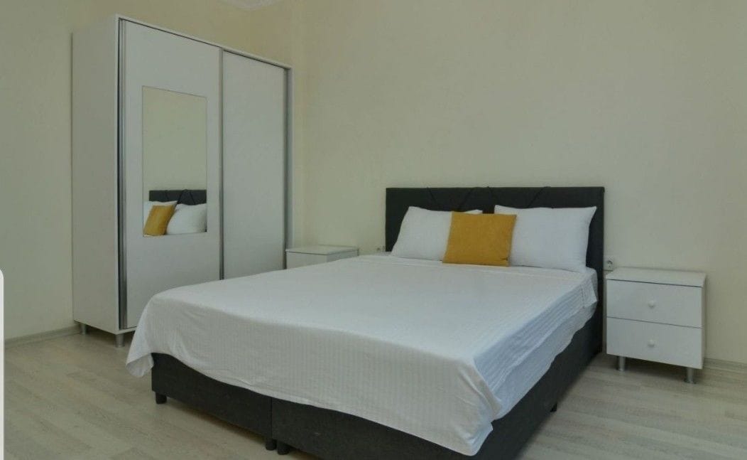 Un dormitorio con cama, mesitas de noche, un armario y un espejo.