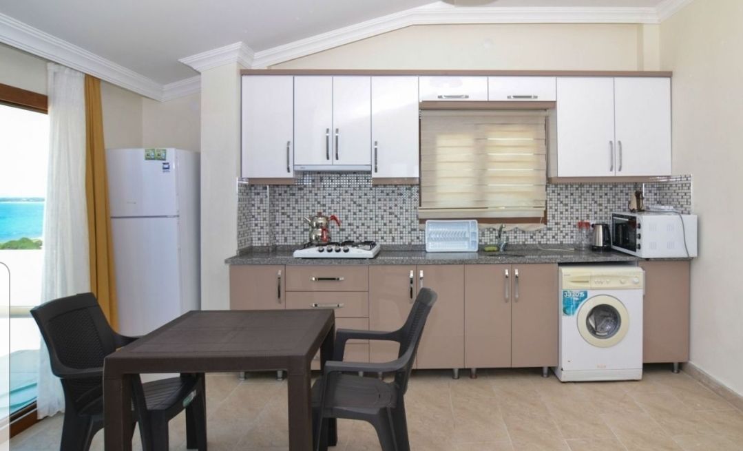 Une cuisine compacte avec un coin repas, un lave-linge et une vue sur la mer.
