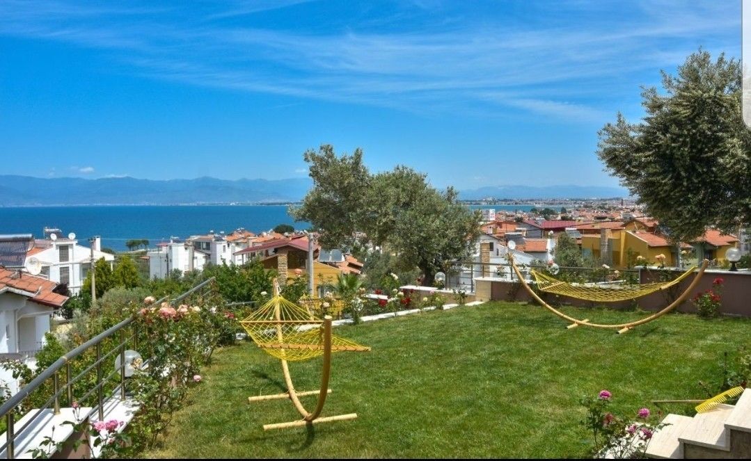 A residential area with a grassy lawn, two hammocks, and a view of the sea and distant mountains.