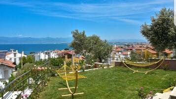 A residential area with a grassy lawn, two hammocks, and a view of the sea and distant mountains.