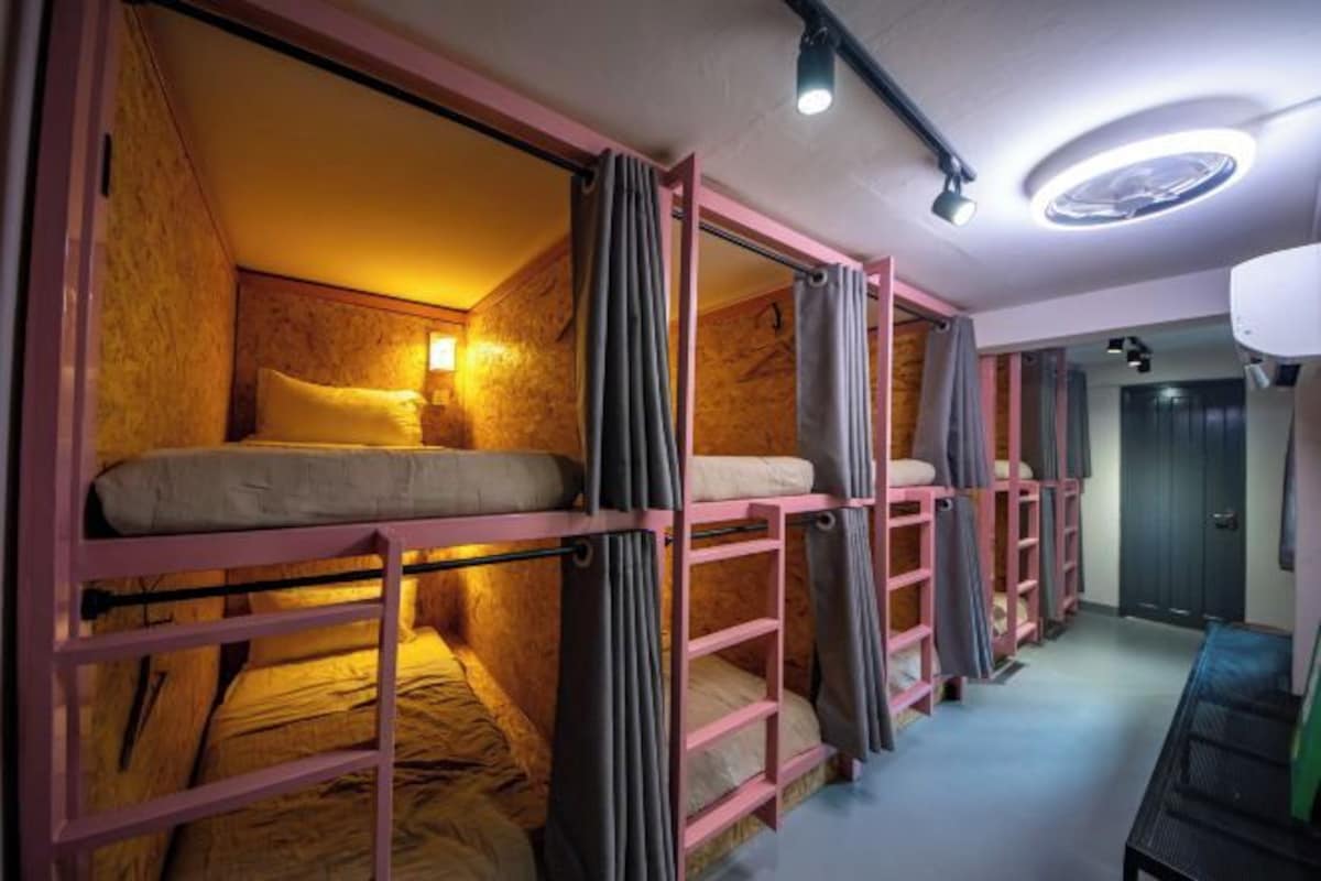 A dormitory room with bunk beds, a ceiling light, and a door.