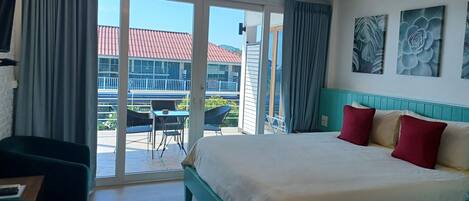 Hotelkamer met een bed, een bureau en een stoel. Er is een balkon met uitzicht op gebouwen en een gebouw met een rood dak.