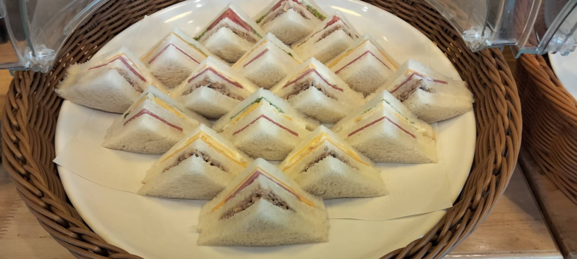 A plate of triangular sandwiches arranged in a diamond pattern on a white plate, placed on a woven basket.