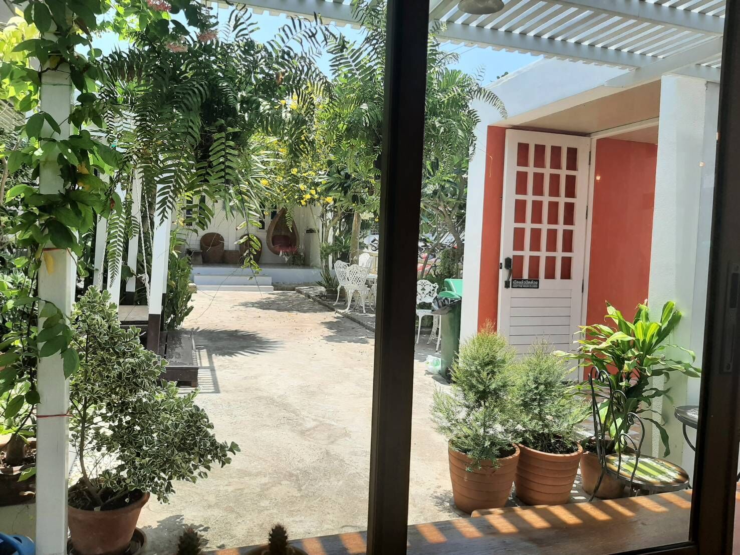 Une cour avec des plantes en pot, une porte blanche et un mur rouge.