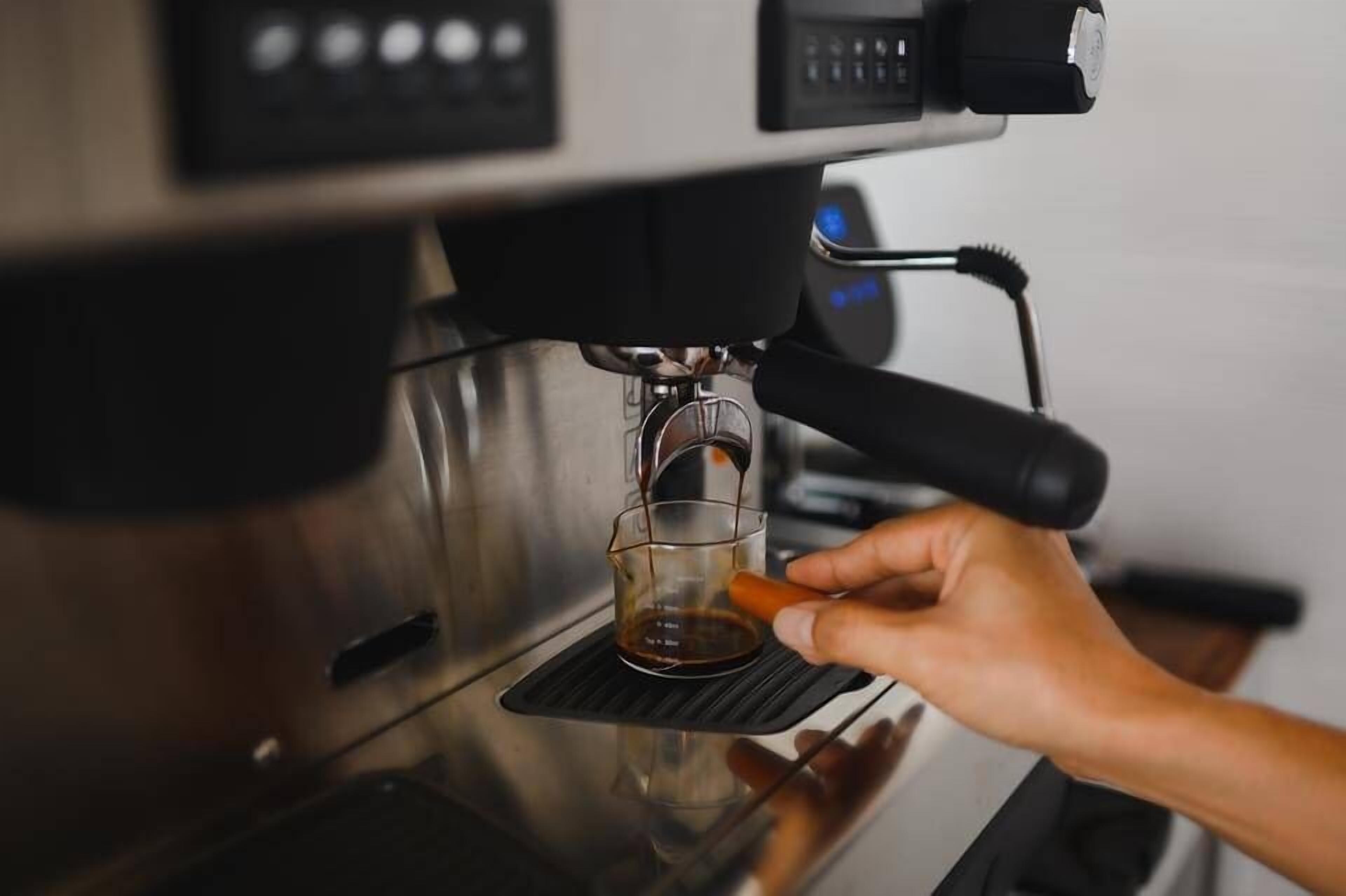Una mano sosteniendo una taza debajo de una máquina de café, con una taza de vidrio transparente en el recipiente colector.